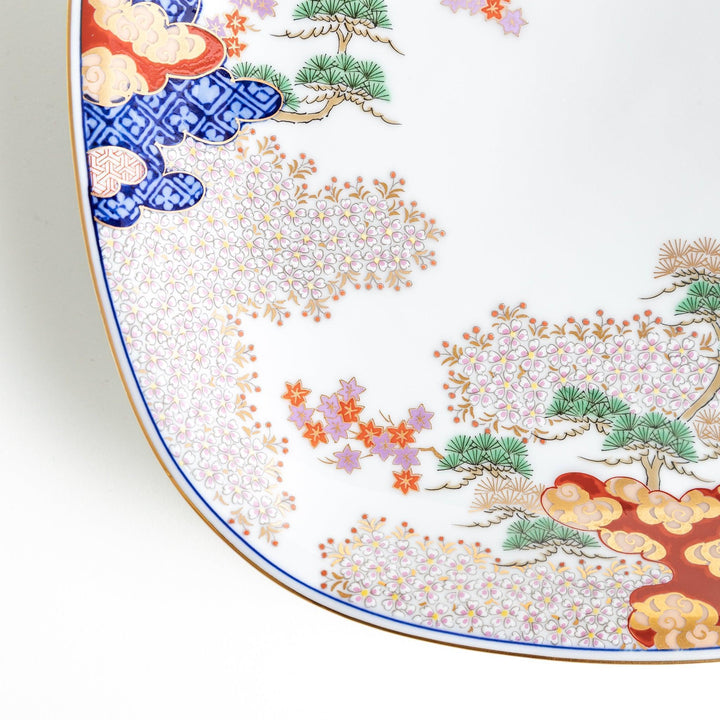 A square serving plate with a white background, decorated with a traditional Japanese landscape of trees, clouds, and red maple leaves.