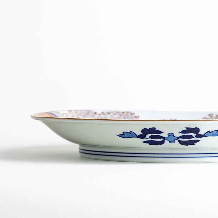 A square serving plate with a white background, decorated with a traditional Japanese landscape of trees, clouds, and red maple leaves.