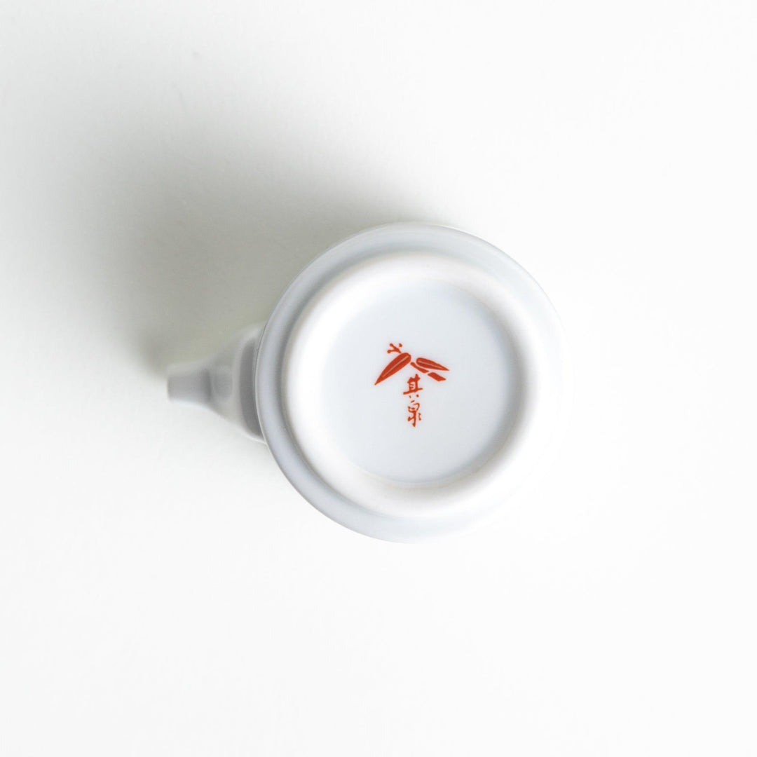 A small white sauce dispenser with intricate traditional Japanese patterns in blue, red, and gold, accompanied by a matching saucer.