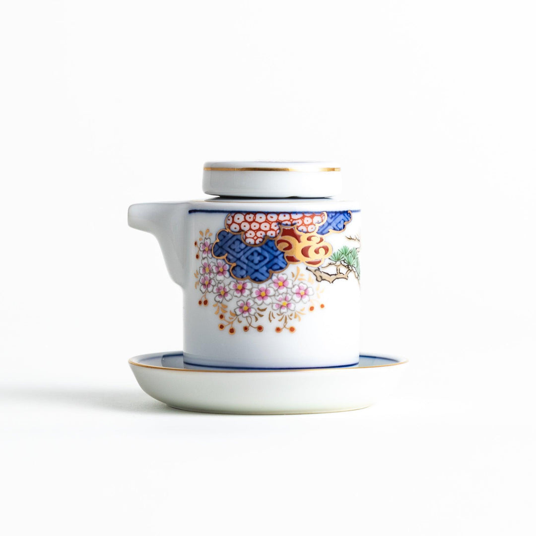 A small white sauce dispenser with intricate traditional Japanese patterns in blue, red, and gold, accompanied by a matching saucer.