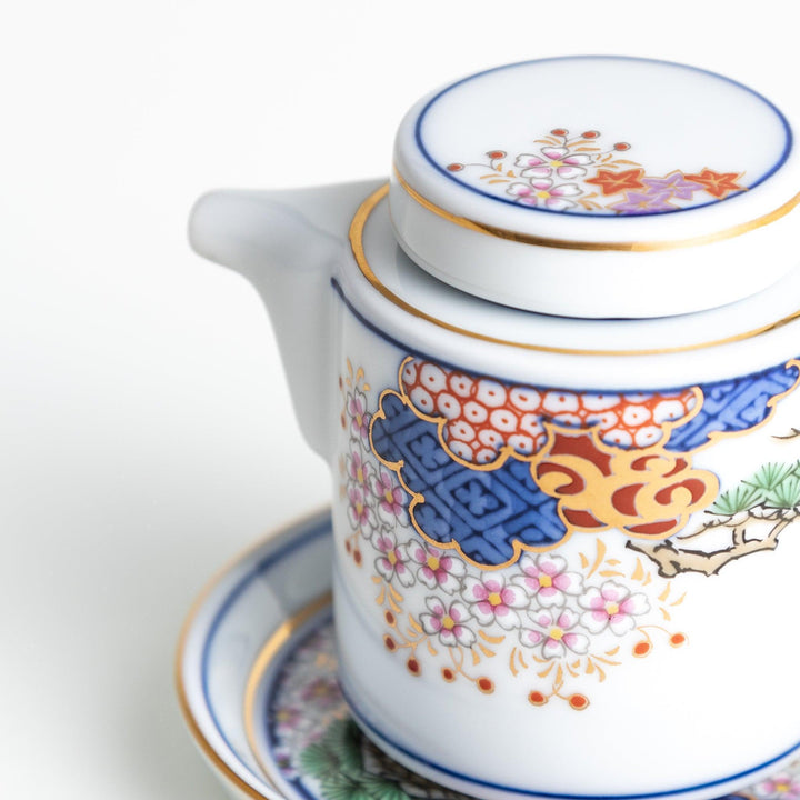 A small white sauce dispenser with intricate traditional Japanese patterns in blue, red, and gold, accompanied by a matching saucer.