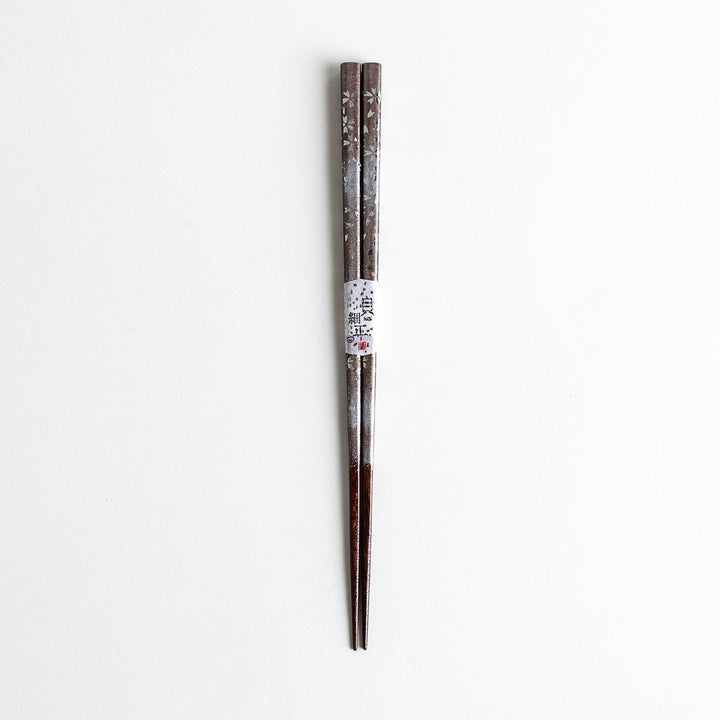 A pair of wooden chopsticks with a faded white gradient and delicate flower patterns near the top.