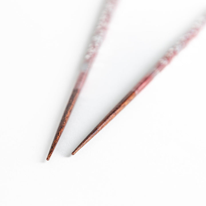 A pair of wooden chopsticks with a faded white gradient and delicate flower patterns near the top.