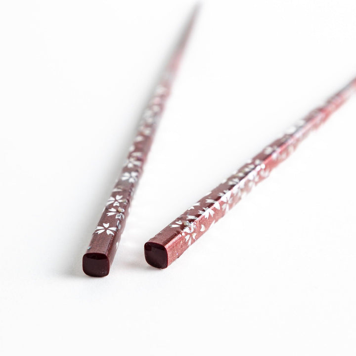 A pair of wooden chopsticks with a faded white gradient and delicate flower patterns near the top.