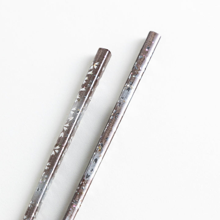 A pair of wooden chopsticks with a faded white gradient and delicate flower patterns near the top.