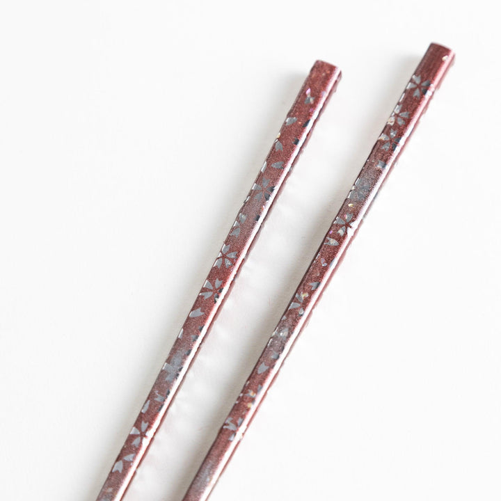 A pair of wooden chopsticks with a faded white gradient and delicate flower patterns near the top.