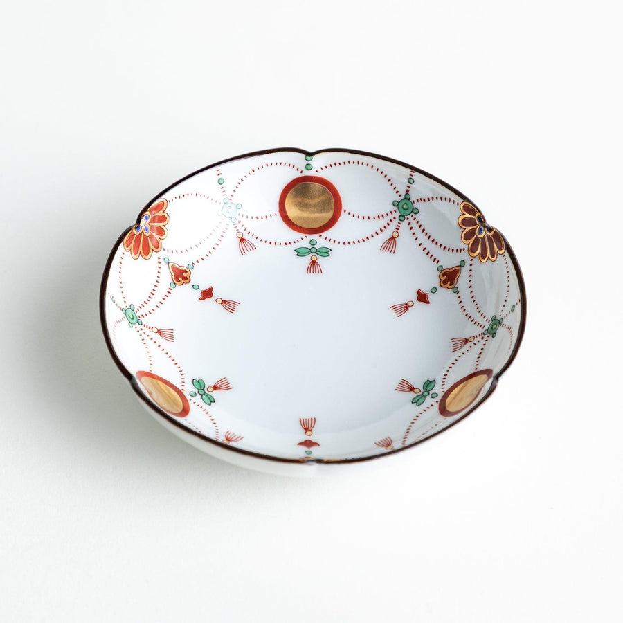 A round white sauce dish with delicate floral and ribbon patterns in gold, green, and red, accented by small scalloped edges.