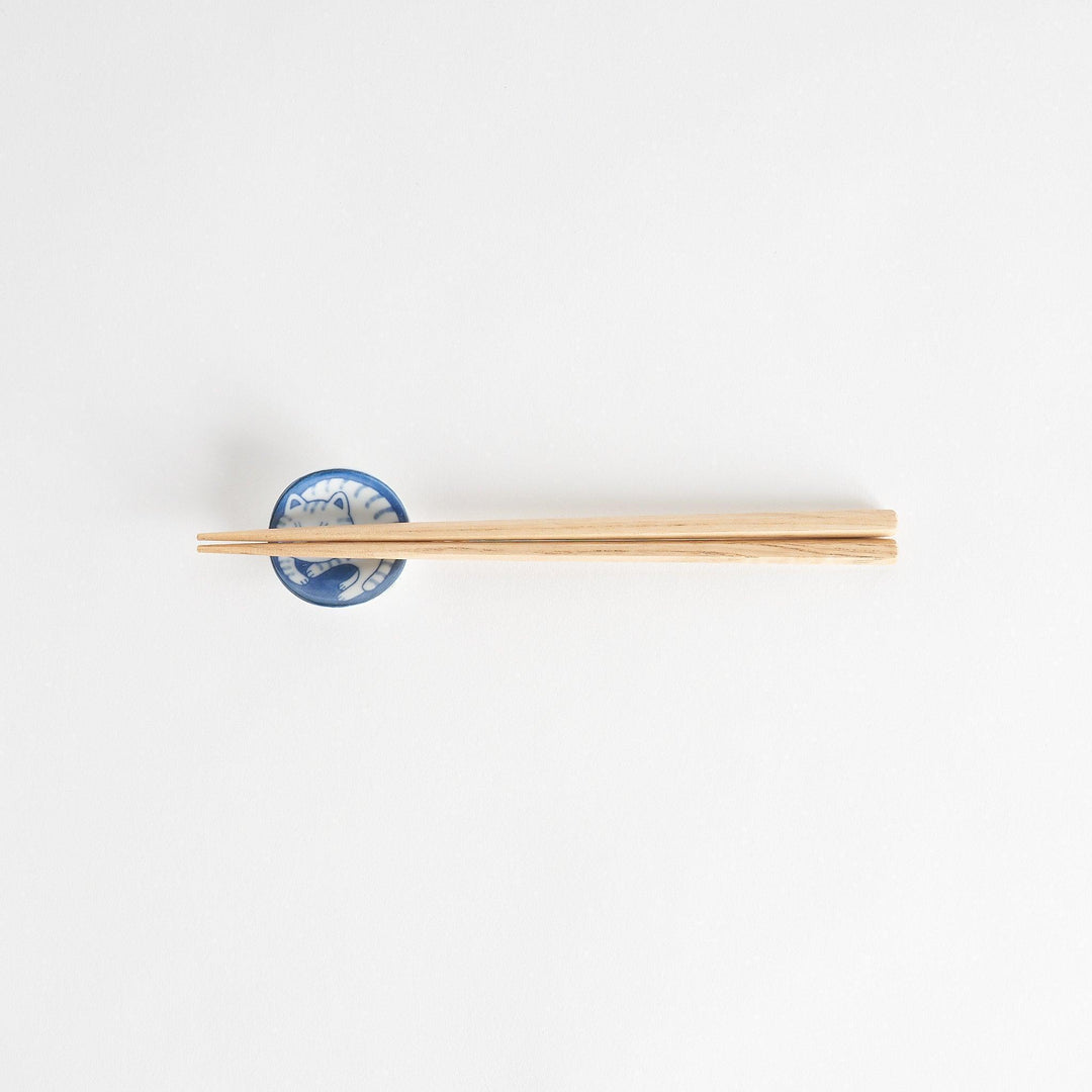 A small chopstick rest featuring a smiling blue-striped cat, curled up in a cozy position.