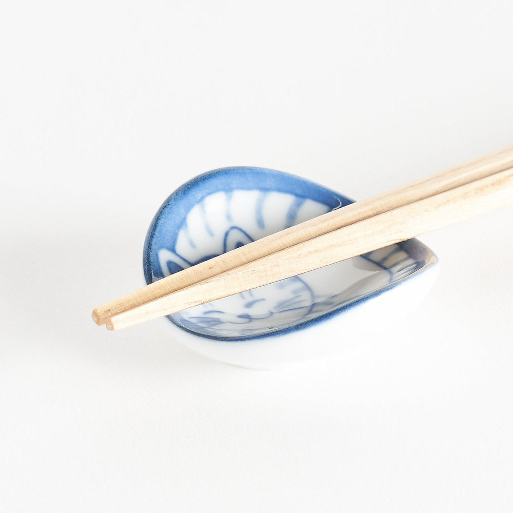 A small chopstick rest featuring a smiling blue-striped cat, curled up in a cozy position.