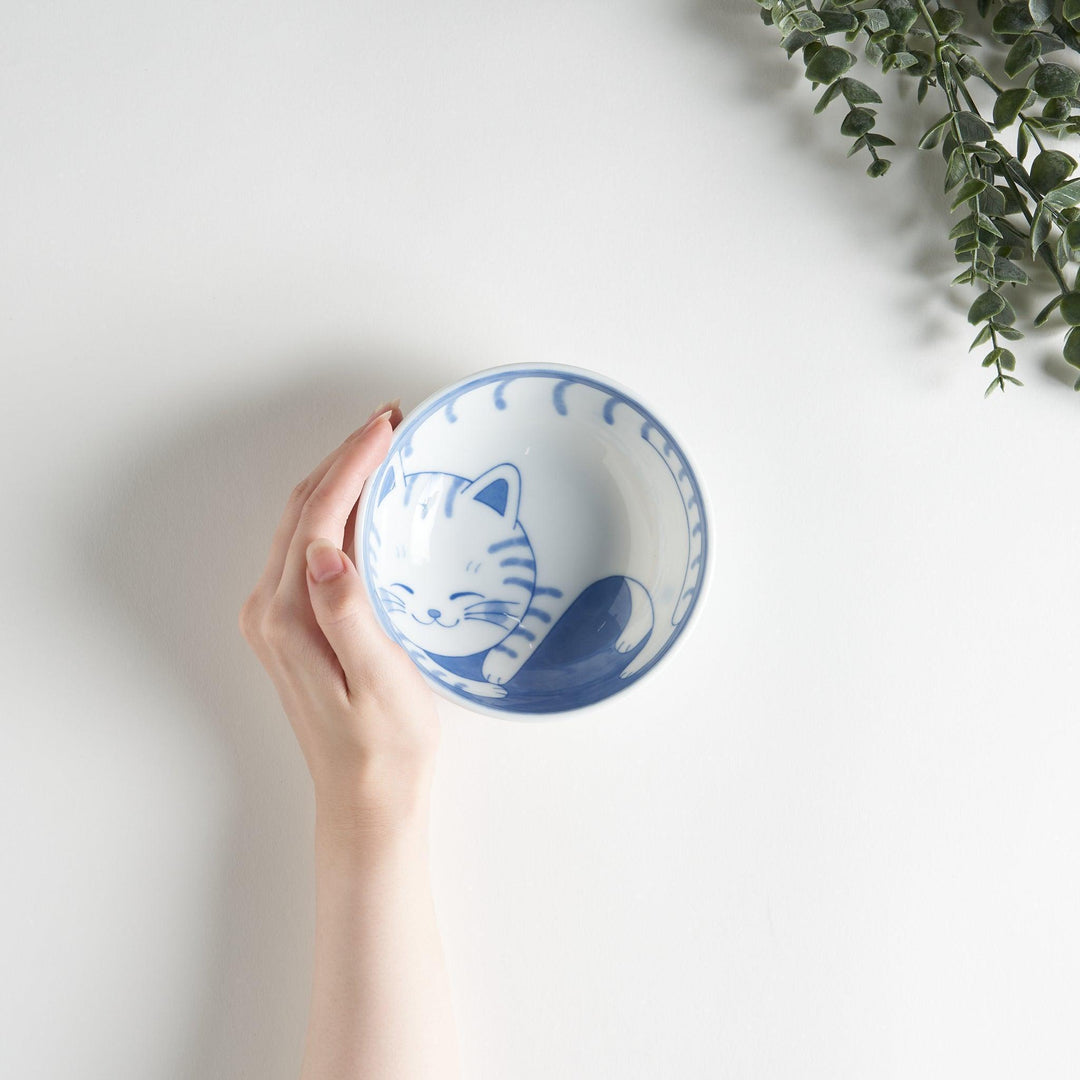 A dessert bowl with a blue-striped cat, smiling contentedly.