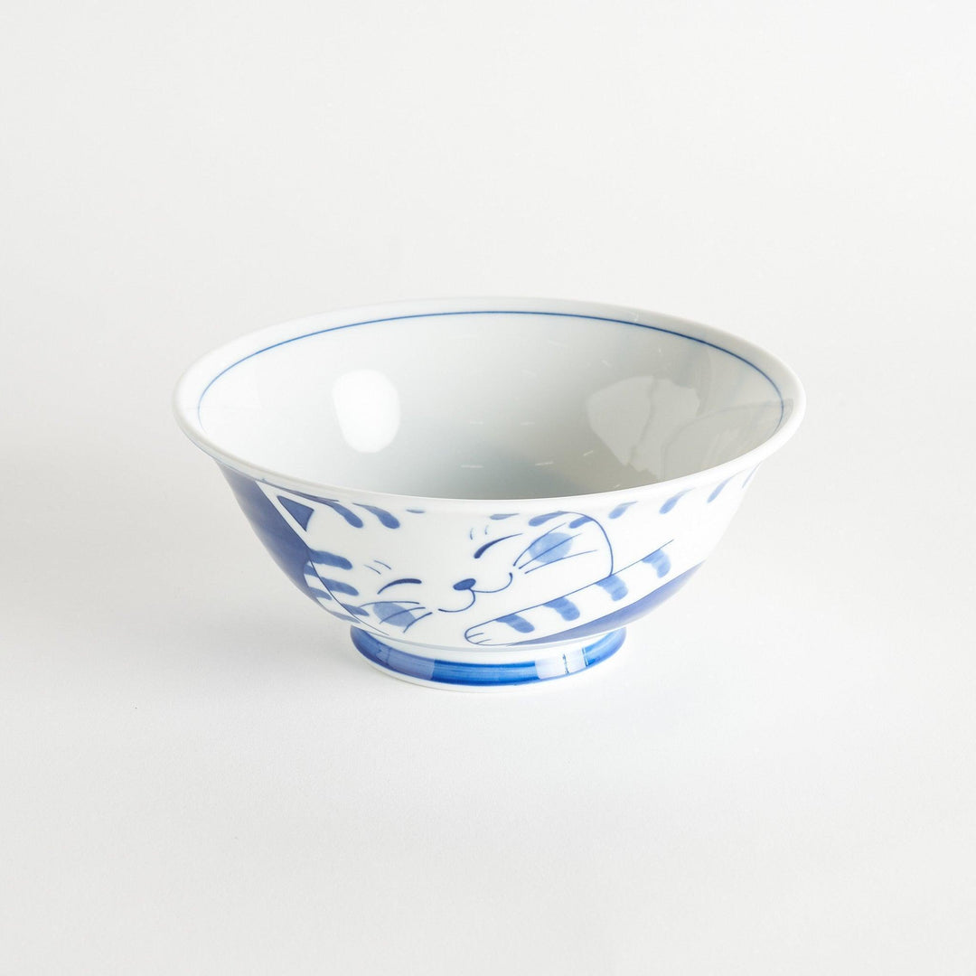 A ramen bowl showcasing a blue and white striped cat stretching out comfortably.