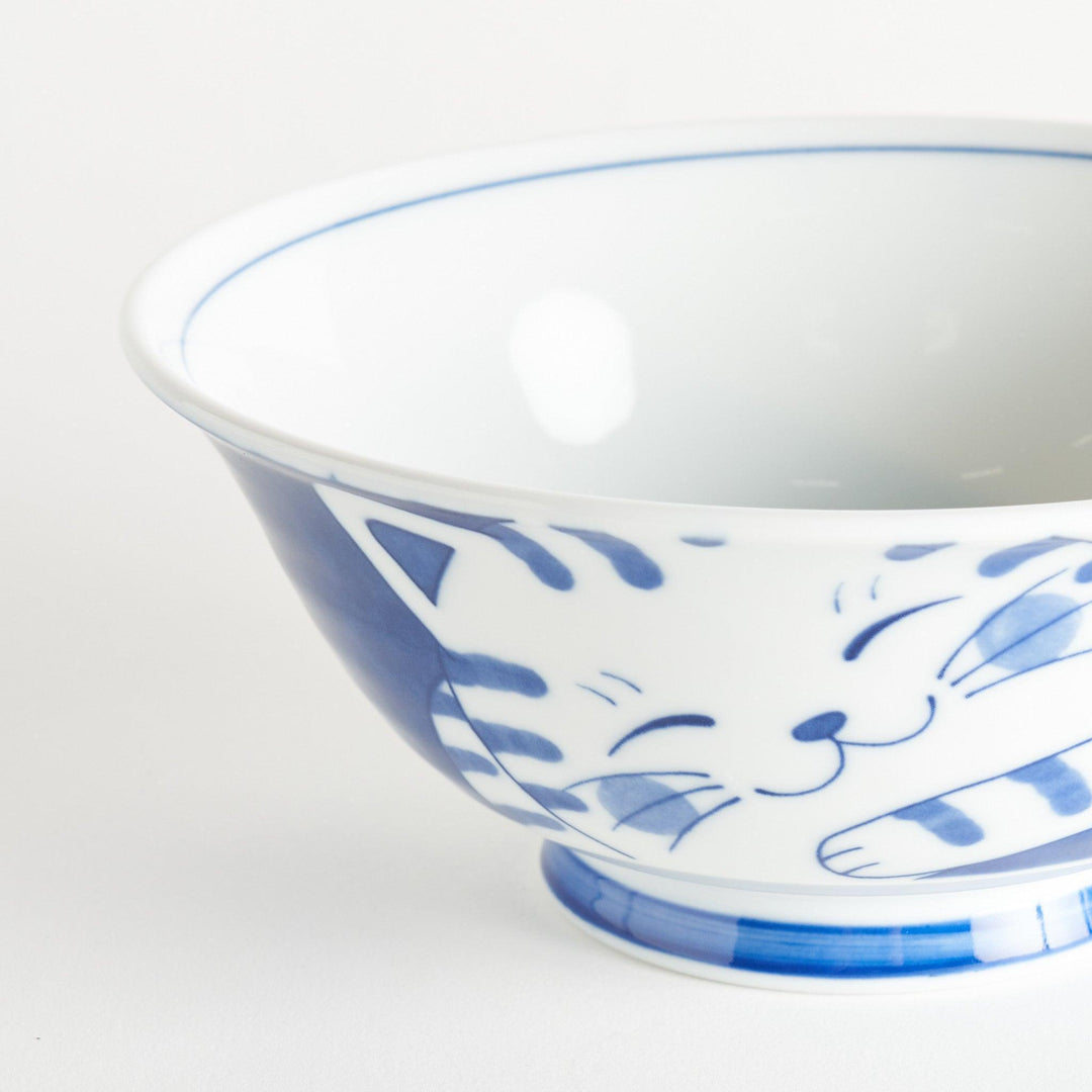 A ramen bowl showcasing a blue and white striped cat stretching out comfortably.