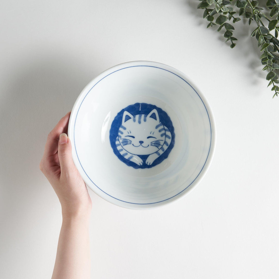 A ramen bowl showcasing a blue and white striped cat stretching out comfortably.