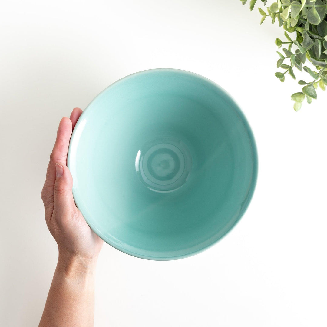 A wide, shallow porcelain bowl with a soft, matte turquoise glaze and subtle horizontal ridges.