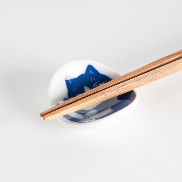 A small chopstick rest featuring a curled-up black and white cat, sleeping peacefully.