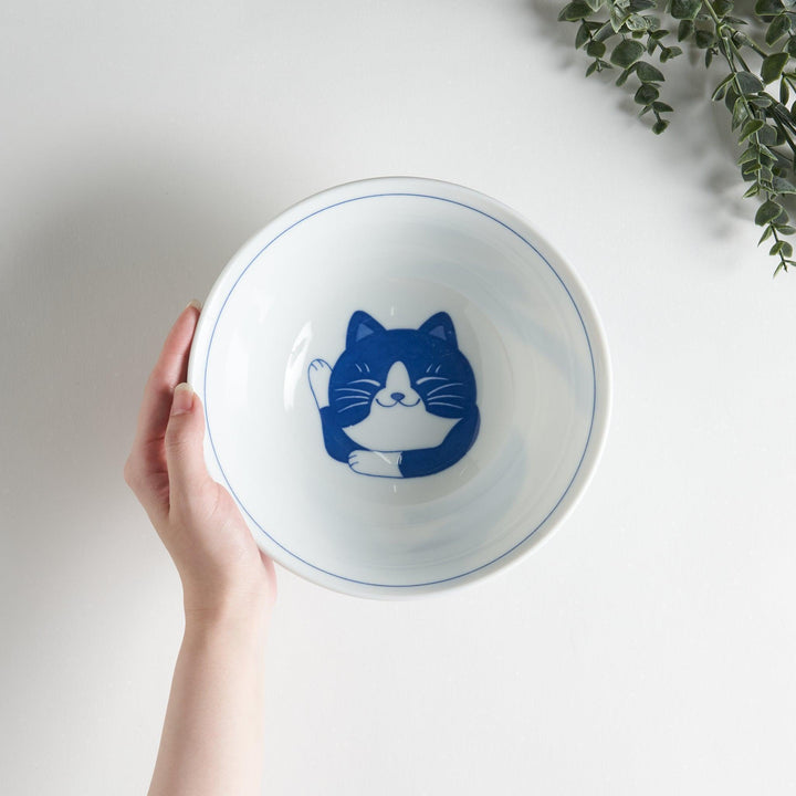 A white ramen bowl featuring a playful blue cat lying down with its eyes closed.