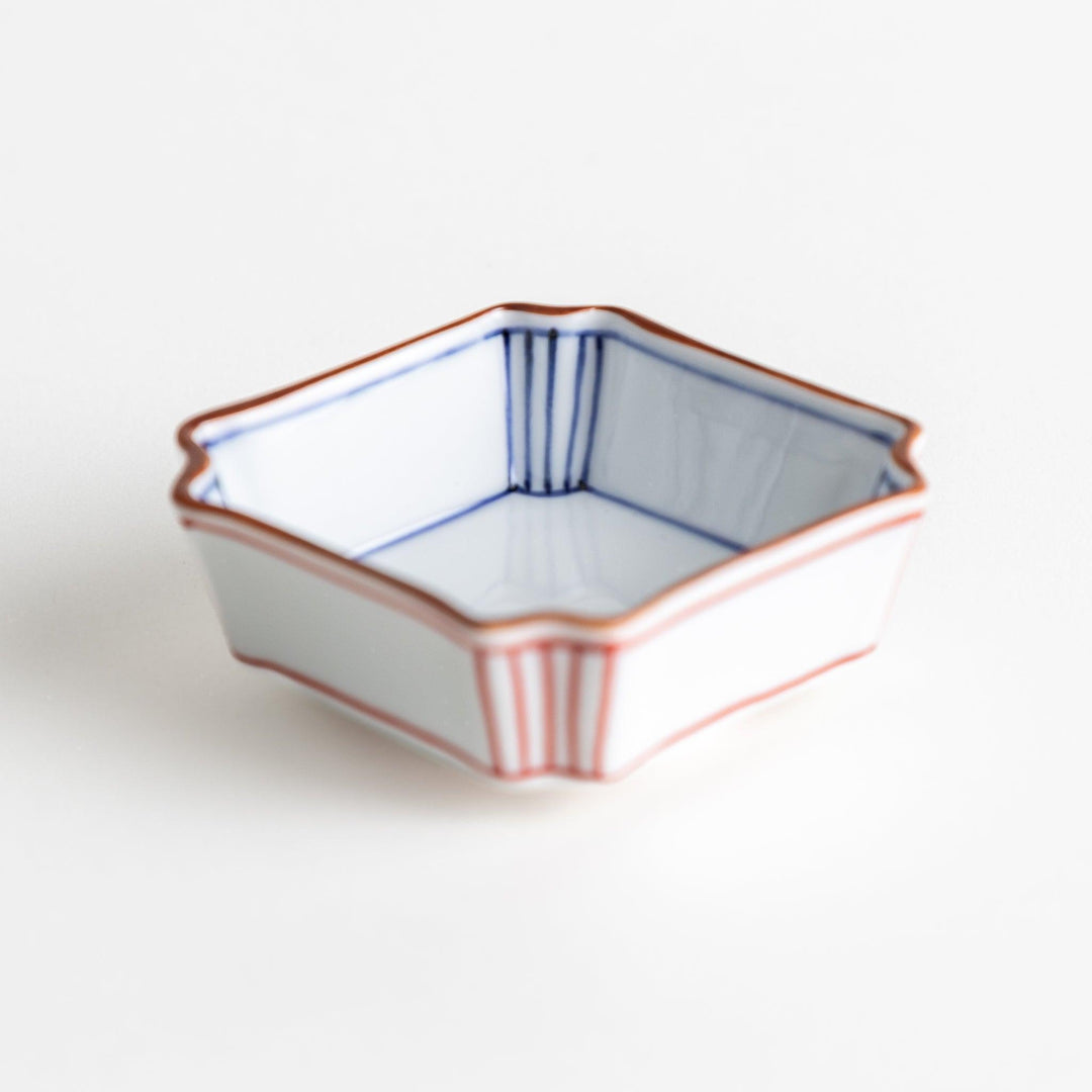 A small square dish with red and blue vertical stripes along the edges, accompanied by a silver spoon.