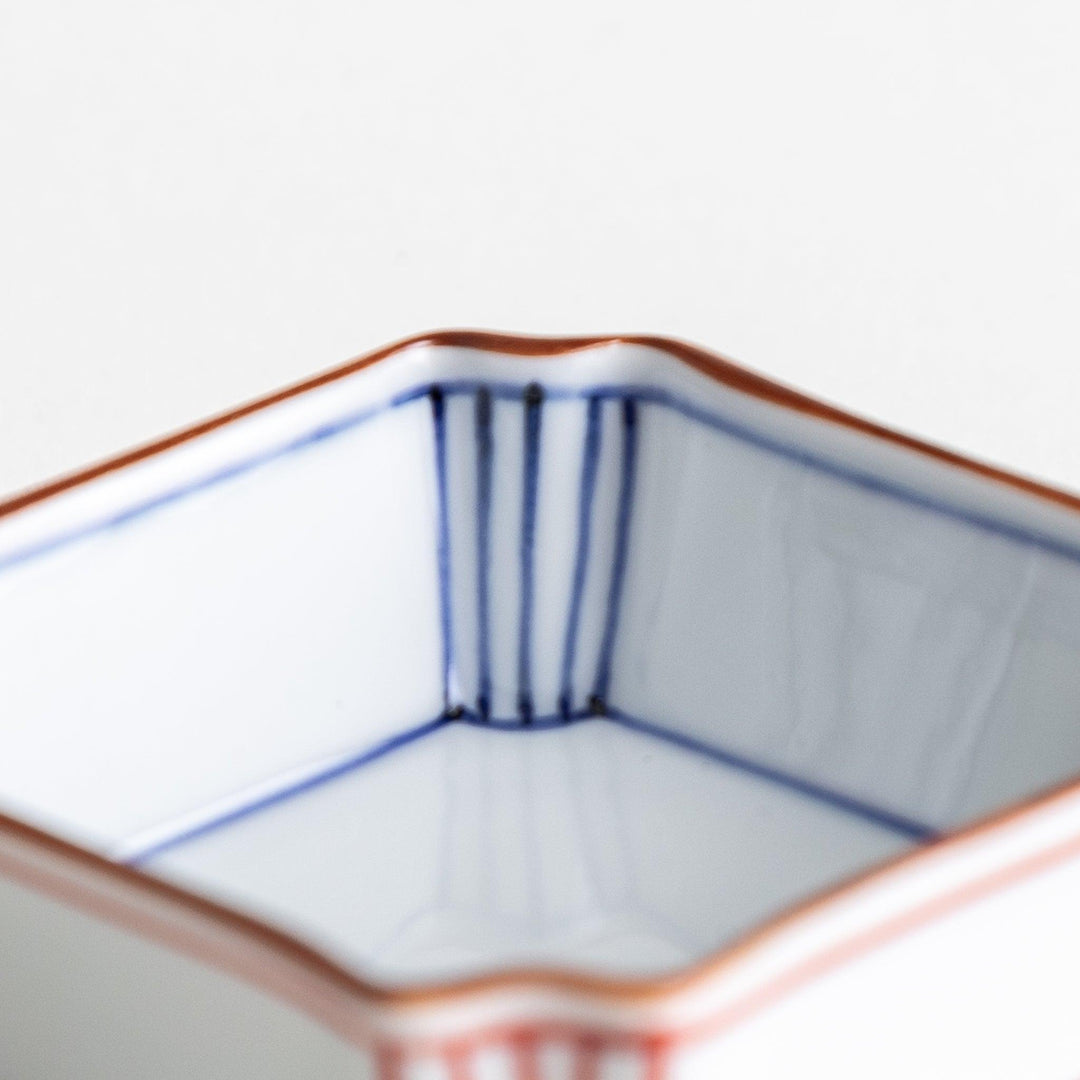 A small square dish with red and blue vertical stripes along the edges, accompanied by a silver spoon.