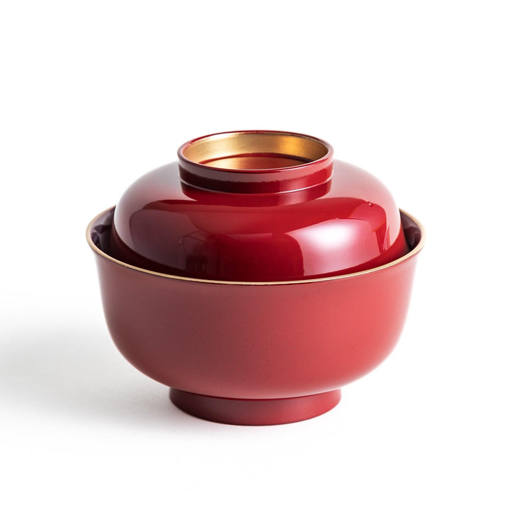 A glossy lacquer bowl with a matching lid, featuring a gold rim around the edge, ideal for serving soups or stews. Available in black or red.