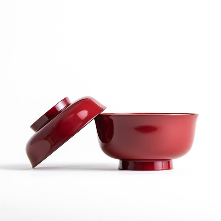 A glossy lacquer bowl with a matching lid, featuring a gold rim around the edge, ideal for serving soups or stews. Available in black or red.