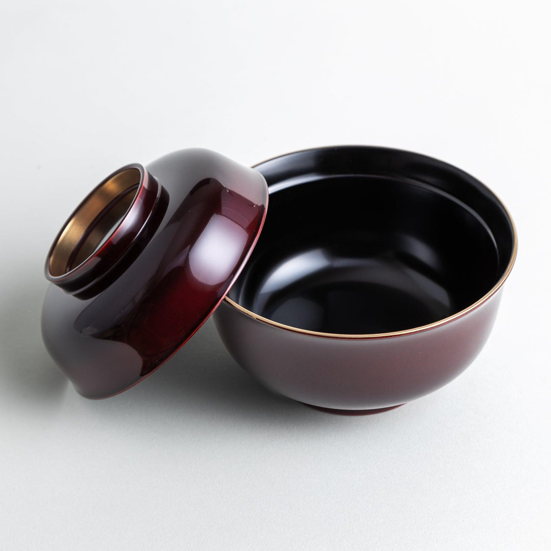 A glossy lacquer bowl with a matching lid, featuring a gold rim around the edge, ideal for serving soups or stews. Available in black or red.