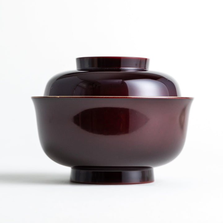 A glossy lacquer bowl with a matching lid, featuring a gold rim around the edge, ideal for serving soups or stews. Available in black or red.