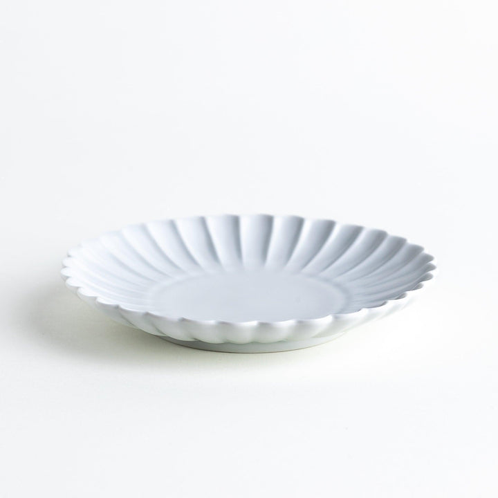 A smaller white porcelain plate with a fluted design, reminiscent of a chrysanthemum flower.