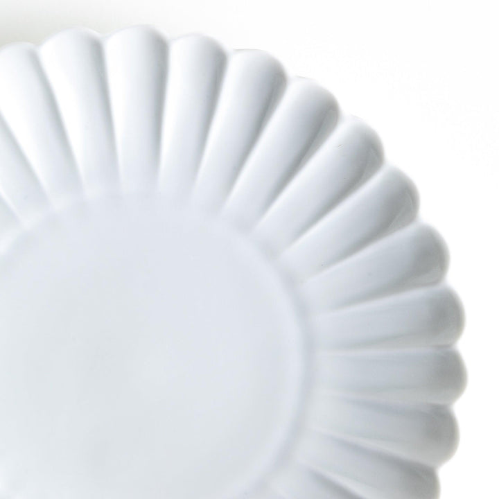 A smaller white porcelain plate with a fluted design, reminiscent of a chrysanthemum flower.