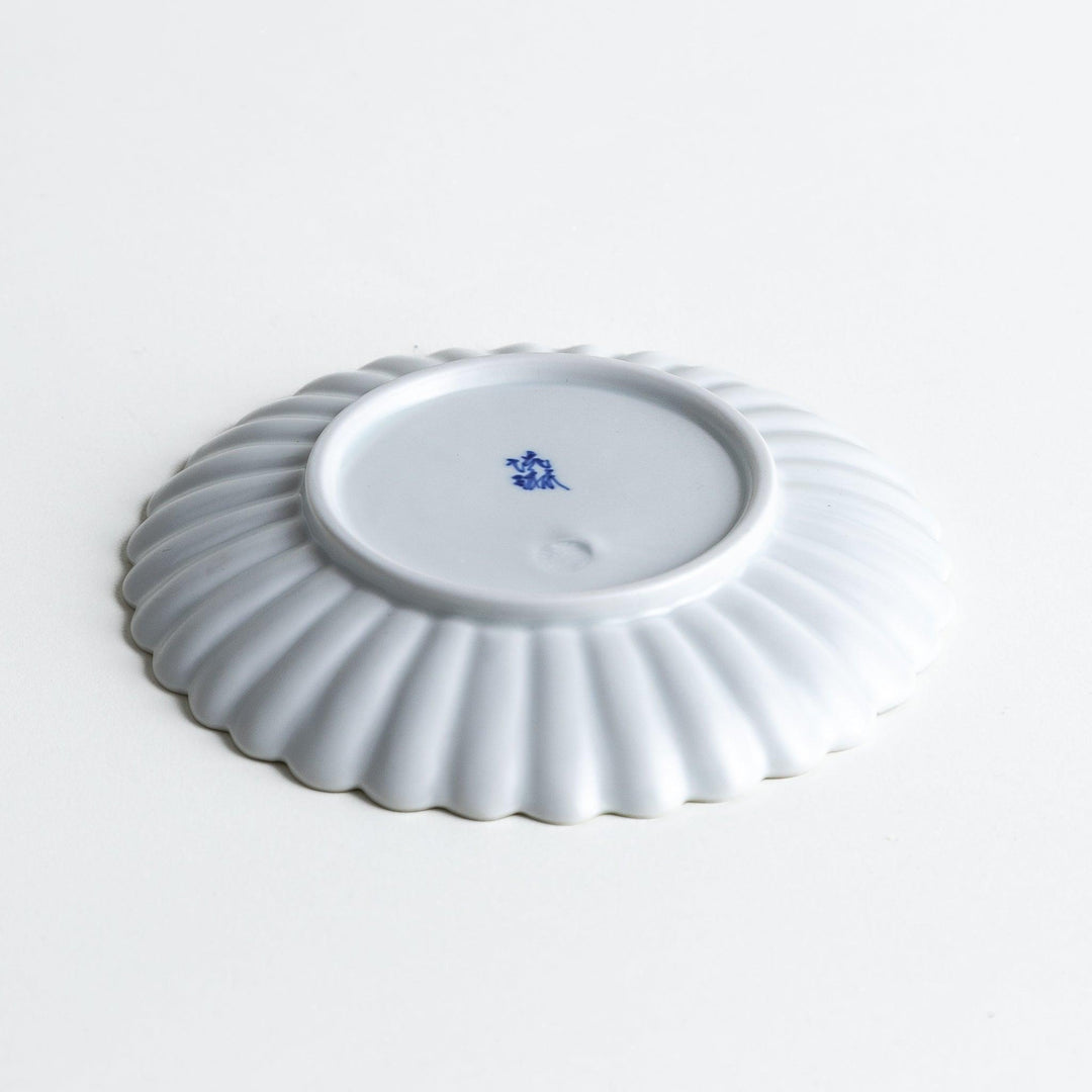 A smaller white porcelain plate with a fluted design, reminiscent of a chrysanthemum flower.