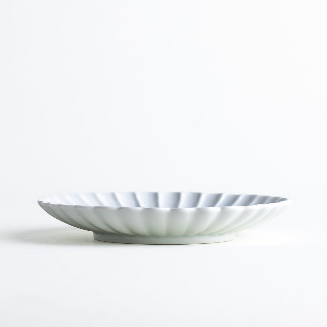 A smaller white porcelain plate with a fluted design, reminiscent of a chrysanthemum flower.