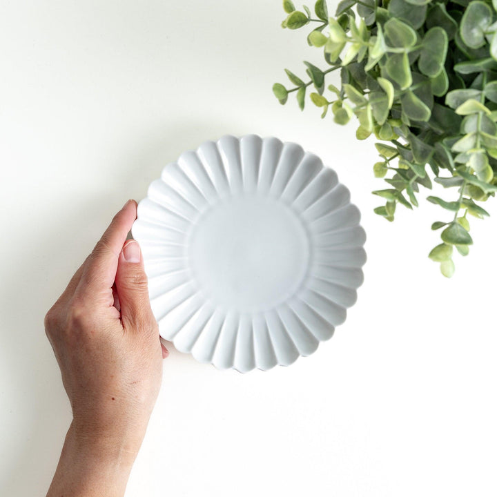 A smaller white porcelain plate with a fluted design, reminiscent of a chrysanthemum flower.