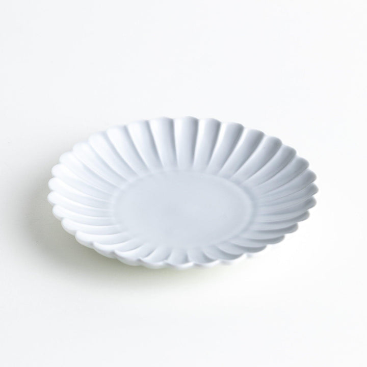 A smaller white porcelain plate with a fluted design, reminiscent of a chrysanthemum flower.