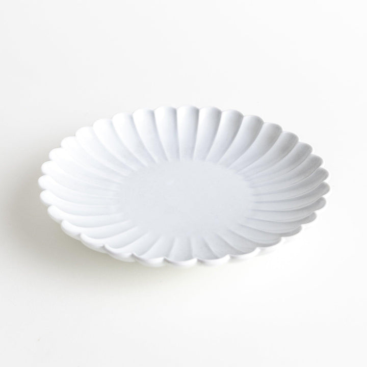 A white porcelain plate with a fluted design, resembling a flower in full bloom.