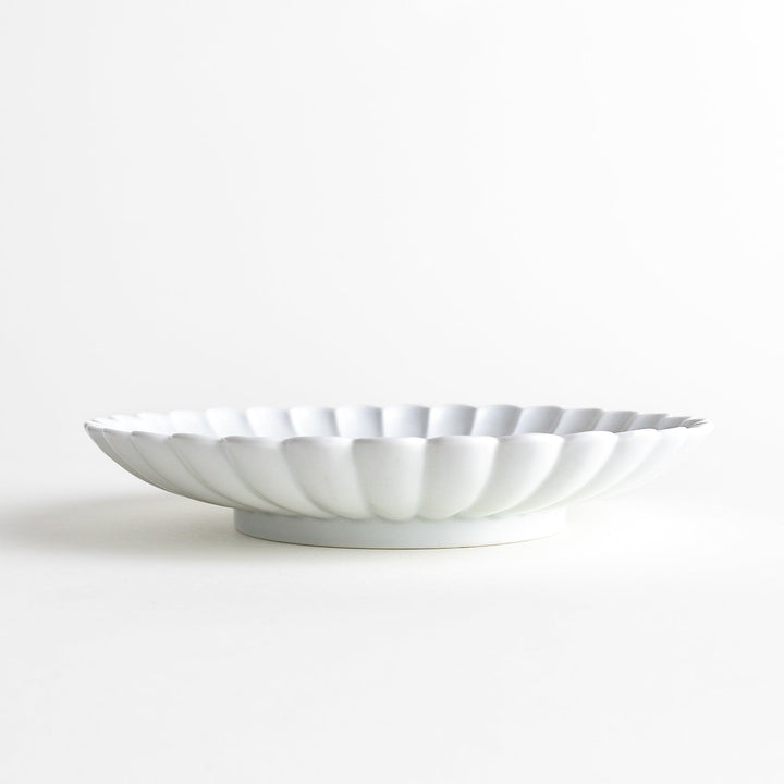 A white porcelain plate with a fluted design, resembling a flower in full bloom.