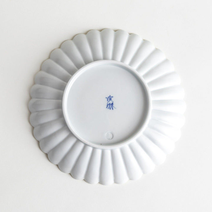 A white porcelain plate with a fluted design, resembling a flower in full bloom.