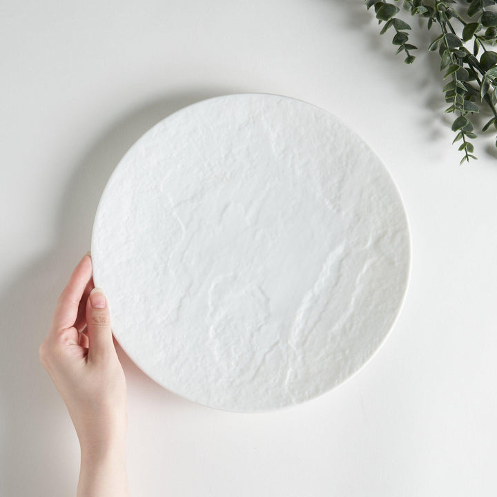 A white luncheon plate featuring a slightly irregular, organic texture and shape, providing a minimalist and natural look.