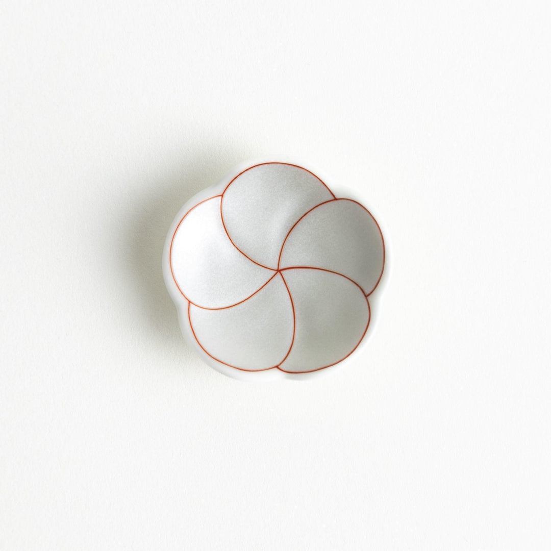 A small, white flower-shaped chopstick rest with a minimalist red swirl pattern.