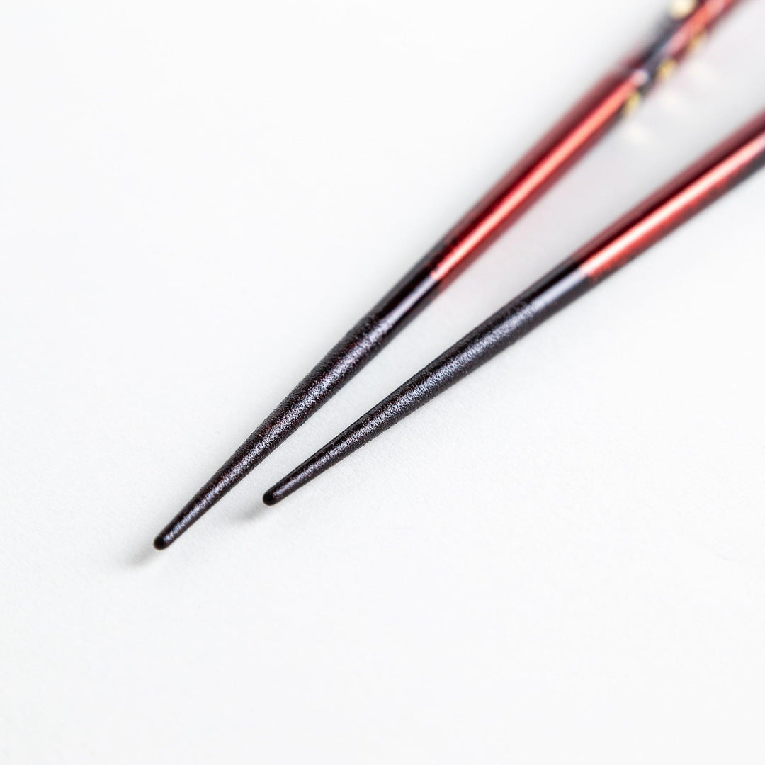 Two pairs of chopsticks in black and red, with golden owl and leaf designs and Japanese text inscriptions.