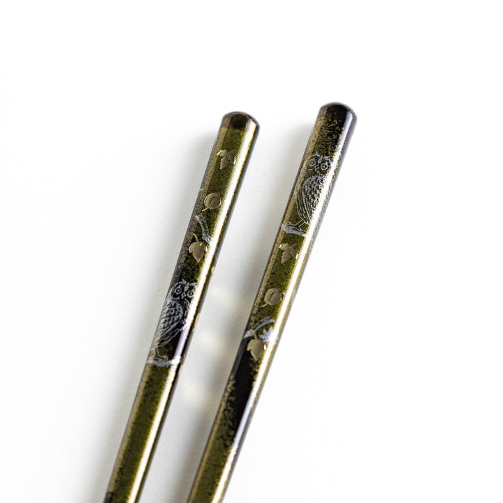 Two pairs of chopsticks in black and red, with golden owl and leaf designs and Japanese text inscriptions.