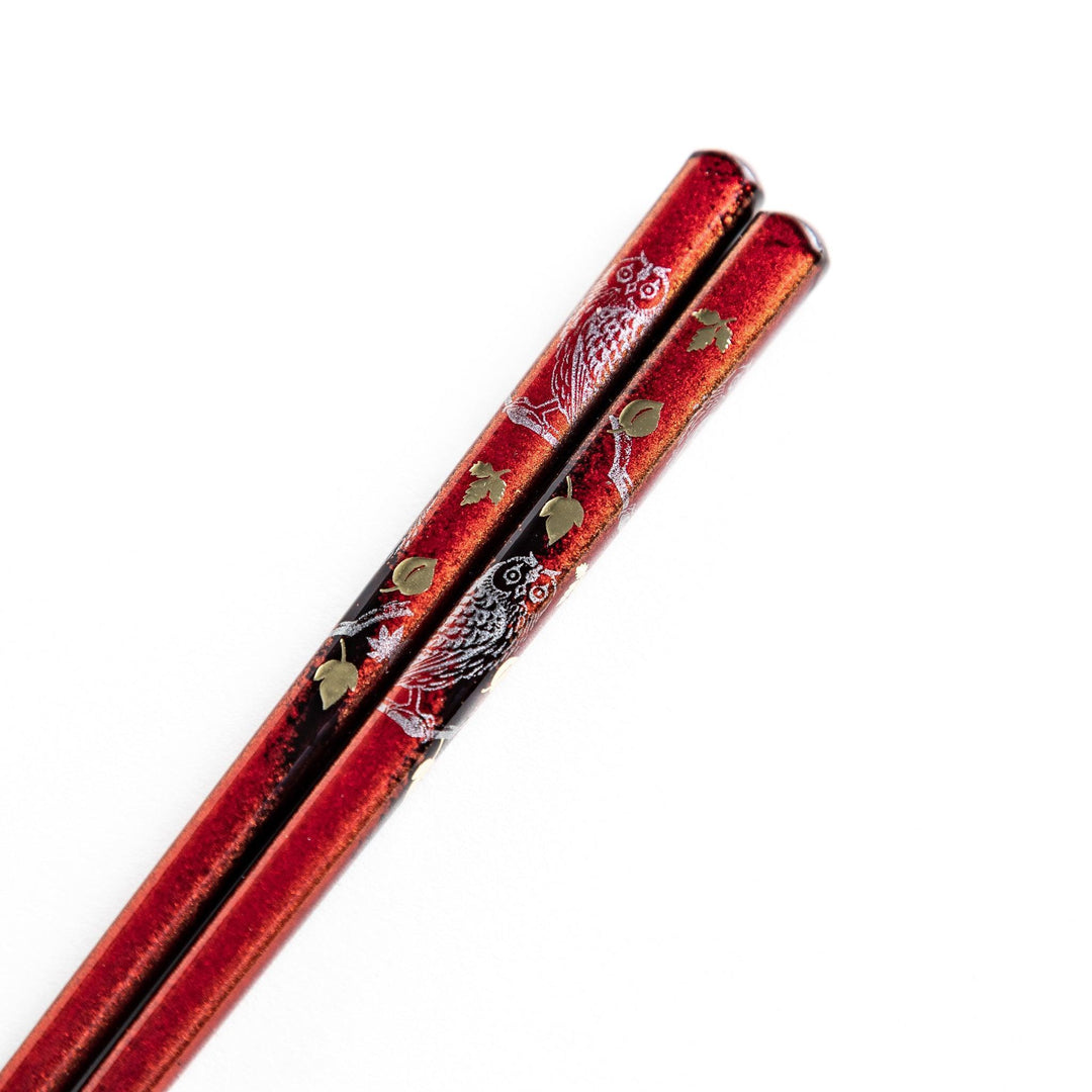 Two pairs of chopsticks in black and red, with golden owl and leaf designs and Japanese text inscriptions.